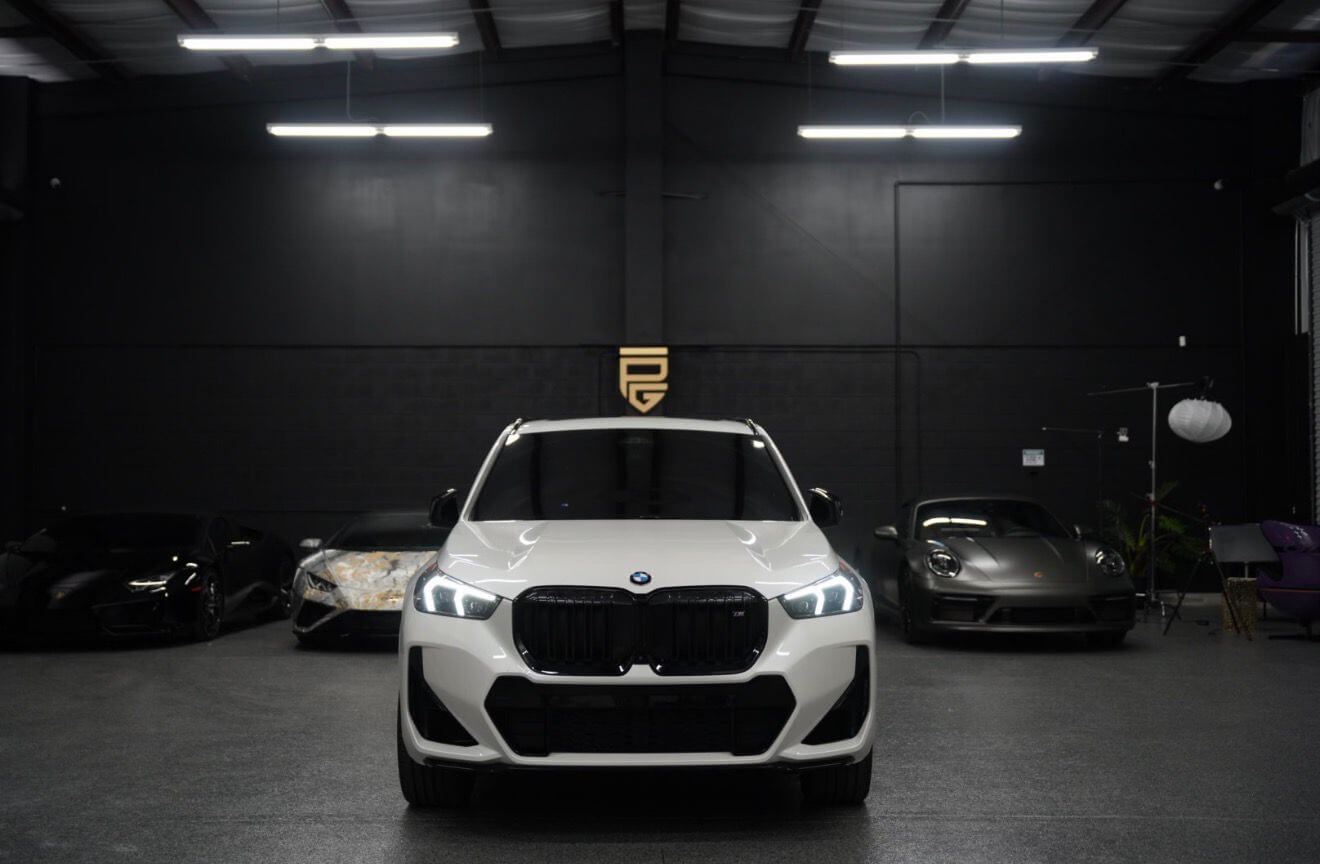 2024 BMW X1 M35i showcased in a luxury car showroom with modern lighting and sleek vehicles in the background.