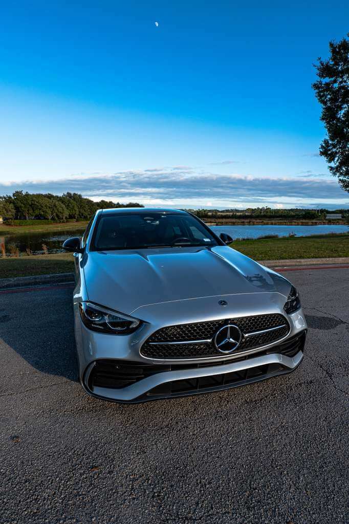 2024 Mercedes C300 in silver parked by the waterfront under a clear blue sky.