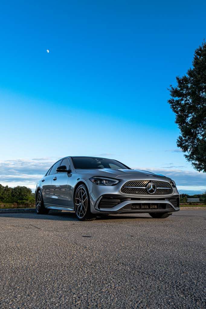 2024 Mercedes C300 parked in scenic landscape under blue sky with trees.