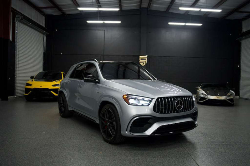 2024 Mercedes GLE 63S in grey parked in luxury showroom with sports cars in background.
