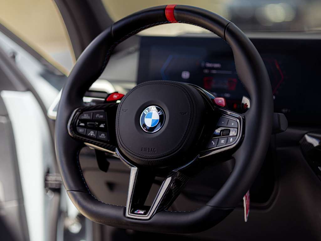 Steering wheel of a 2026 BMW M3 Competition featuring luxury controls and BMW logo.