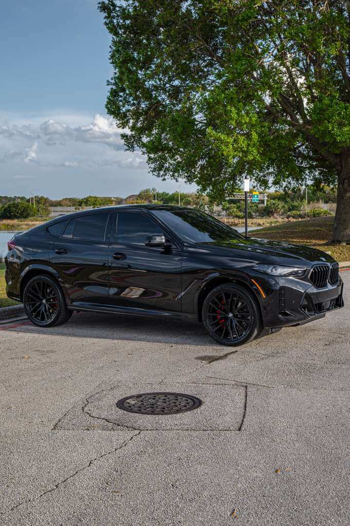 2026 BMW X6 luxury SUV parked on a street surrounded by greenery, showcasing its sleek design.