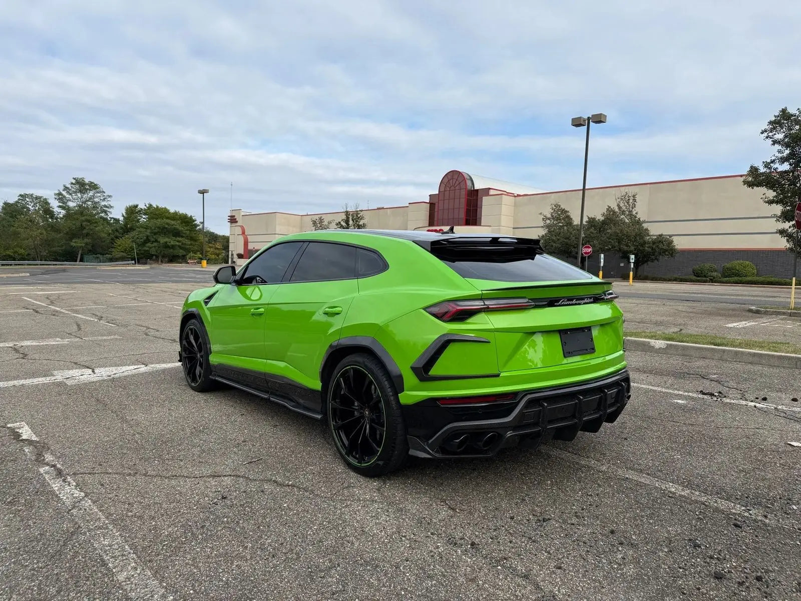 Green Lamborghini Urus luxury SUV with black rims and tinted windows parked in an empty lot, high-performance exotic sports car.