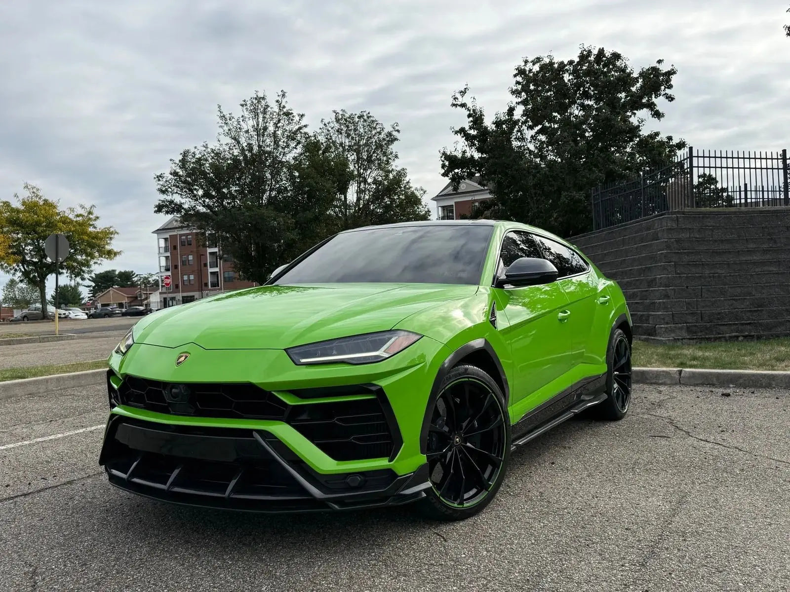 Bright green Lamborghini Urus luxury SUV with black alloy wheels, aerodynamic design, and LED headlights parked outdoors on a cloudy day.