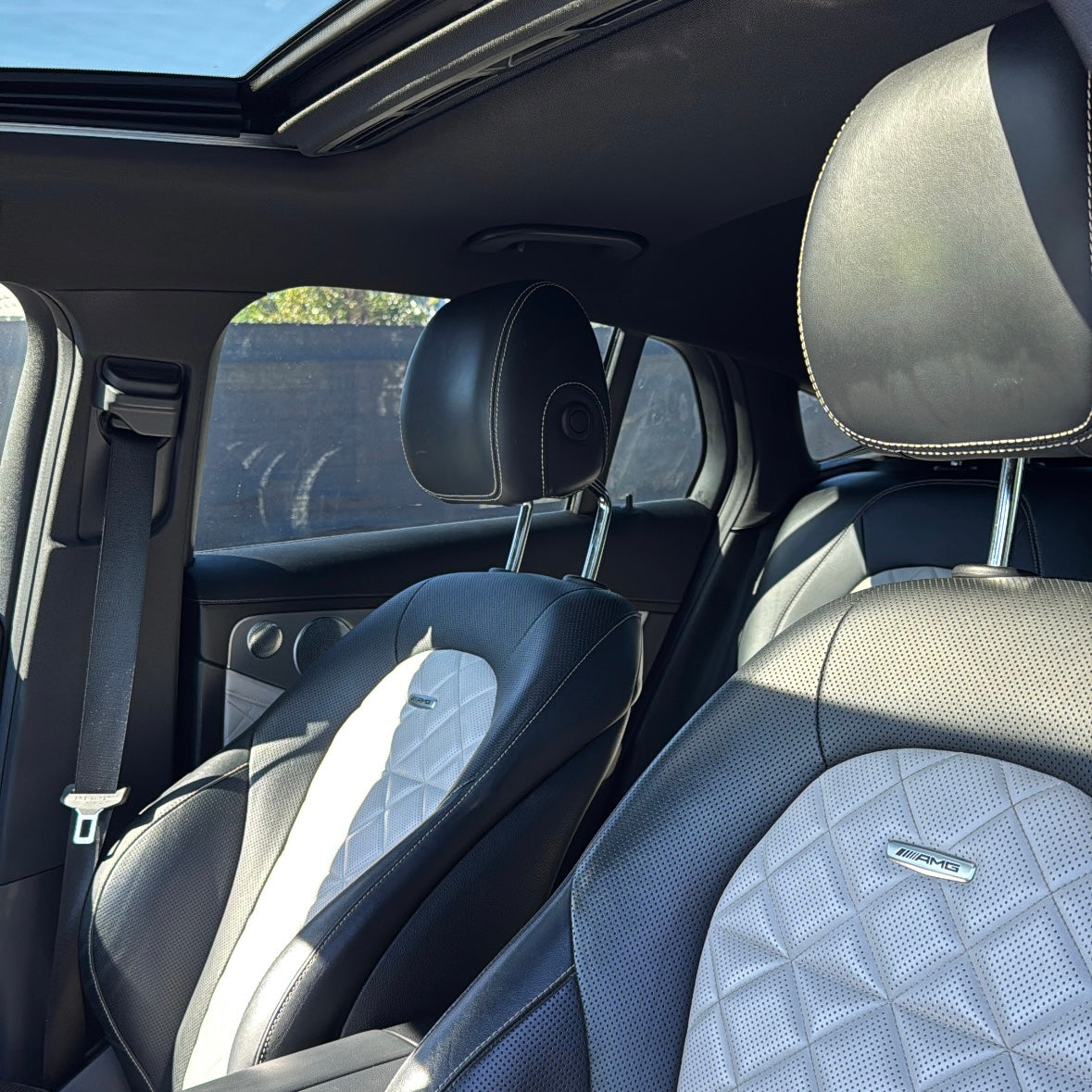 Luxury AMG car interior with black and white perforated leather racing seats and contrast stitching, featuring adjustable headrests and panoramic sunroof.