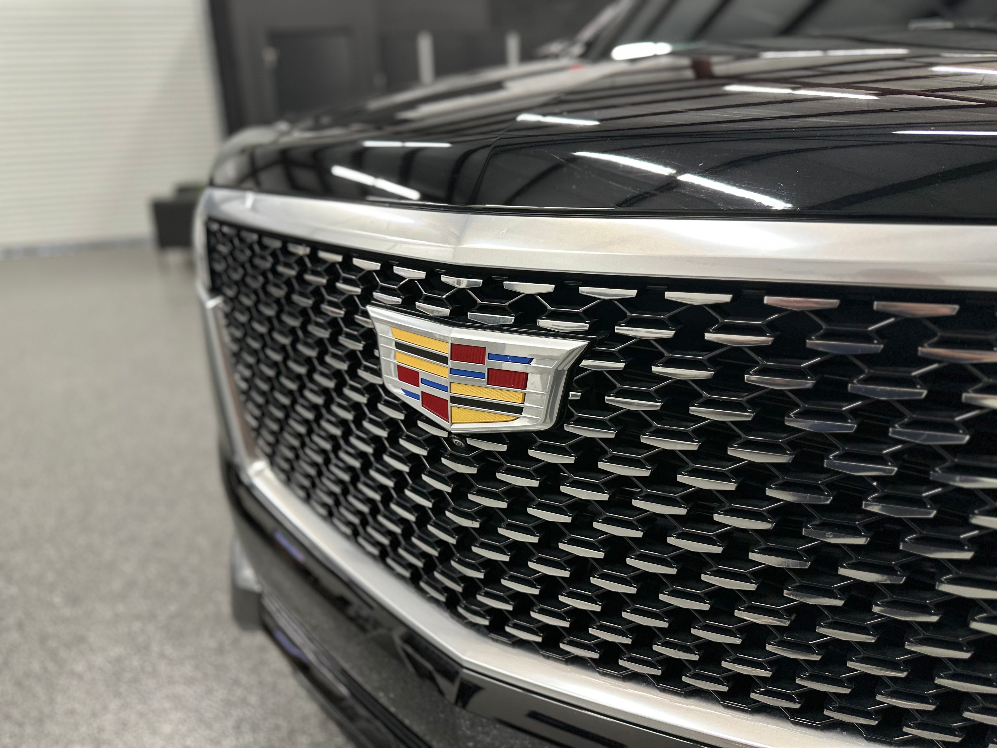 Close-up of black Cadillac vehicle front grille with chrome accents and Cadillac emblem, luxury car exterior detail.