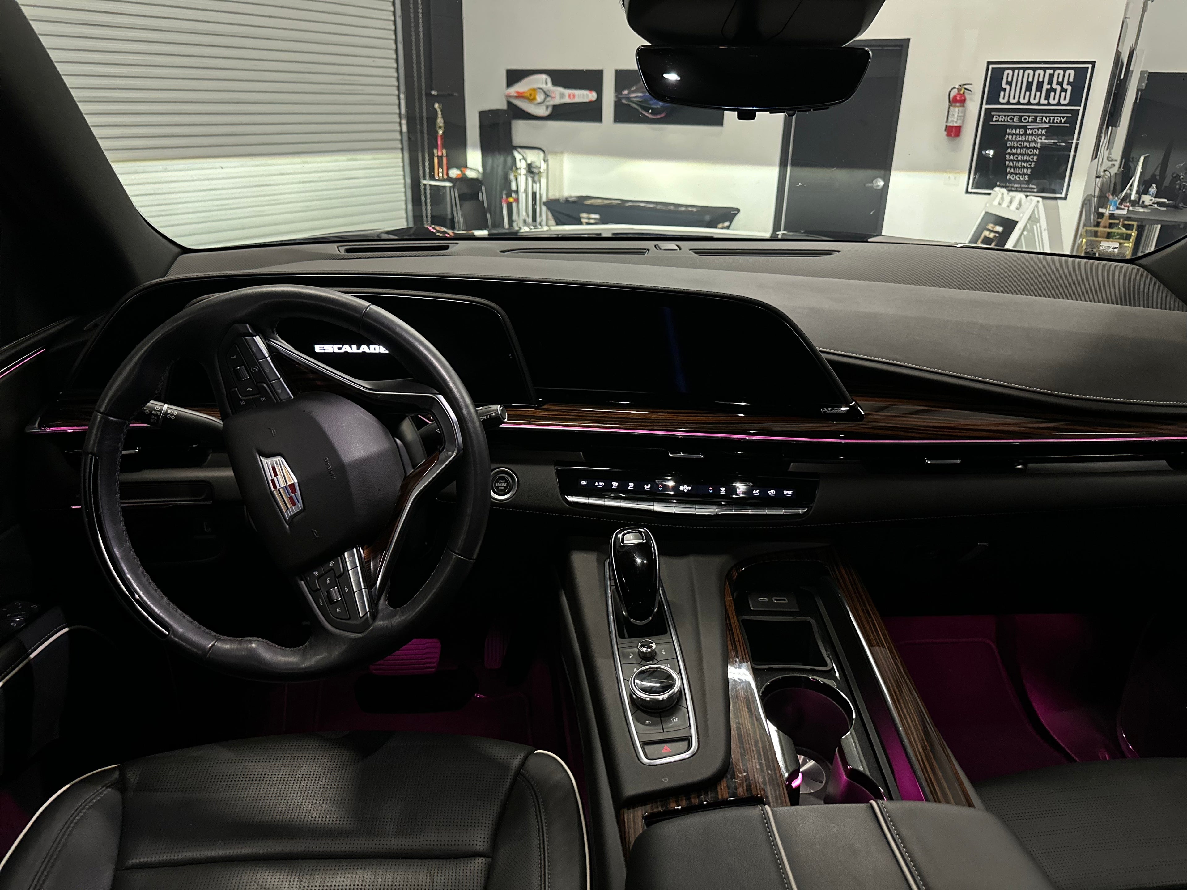Interior view of Cadillac Escalade luxury SUV showing black leather steering wheel, digital dashboard, wood grain trim, and high-tech center console.