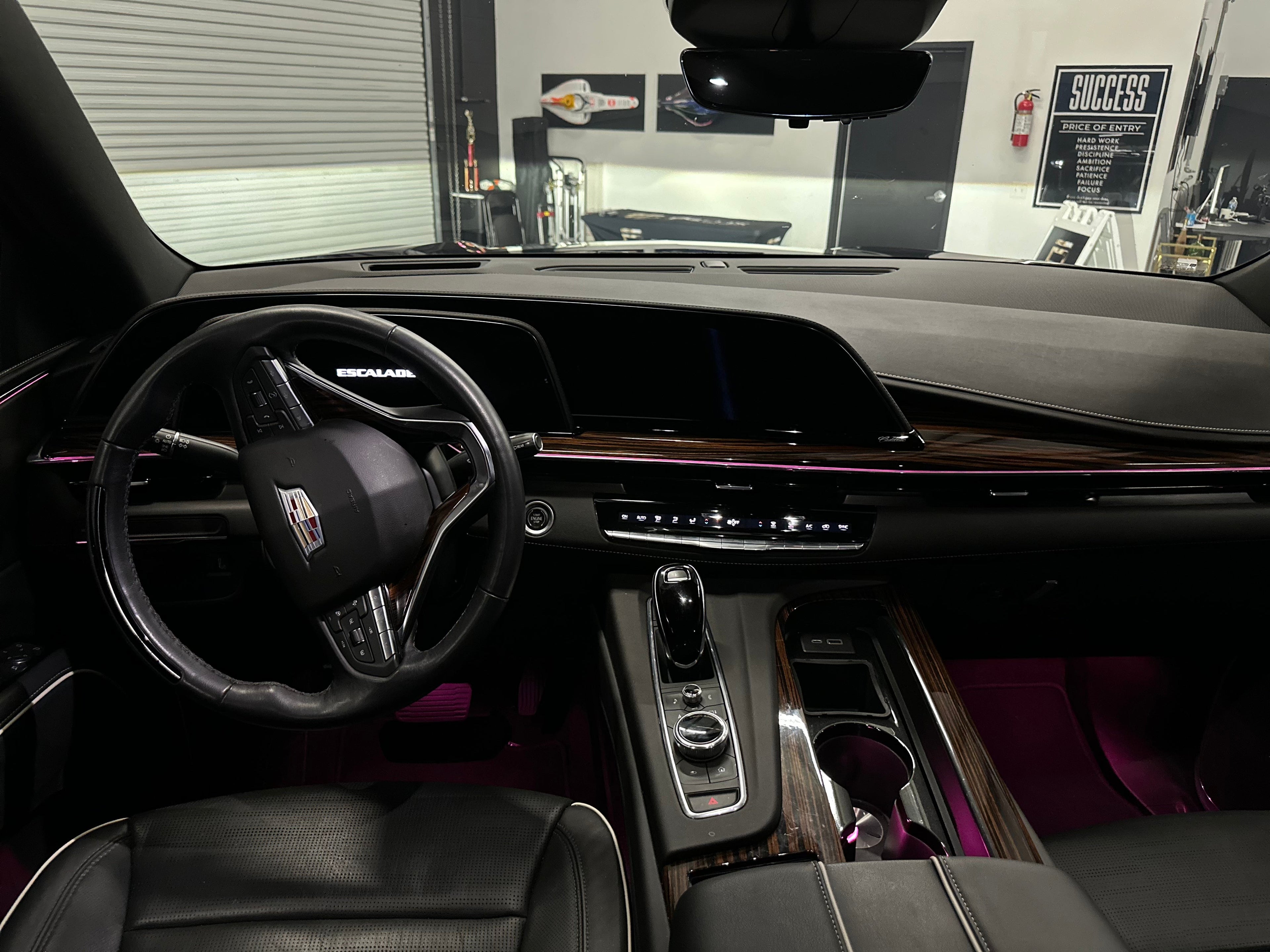 Interior view of Cadillac Escalade luxury SUV showing black leather steering wheel, digital dashboard, wood grain trim, and high-tech center console.