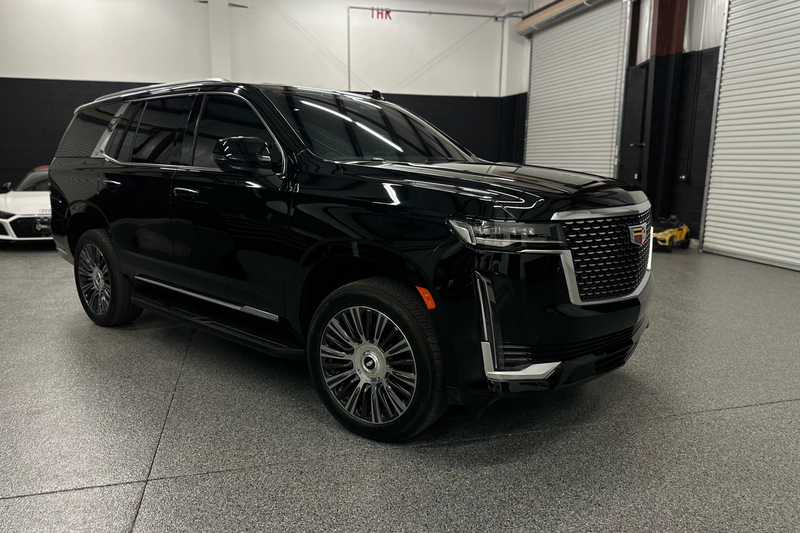Black luxury Cadillac Escalade SUV with chrome grille and alloy wheels in indoor showroom, premium full-size SUV vehicle.
