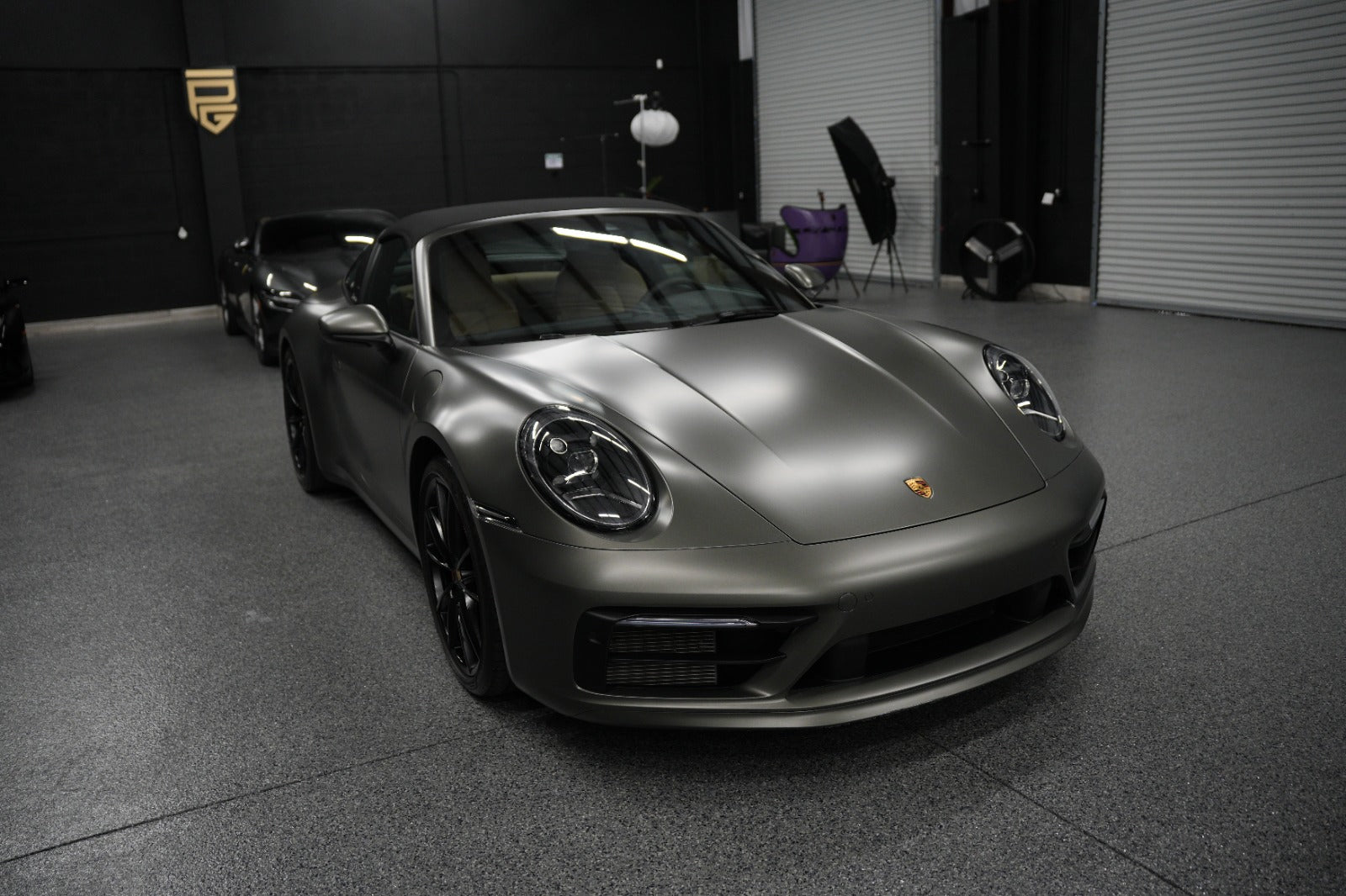 Matte gray Porsche 911 convertible sports car with black rims, showcased in a modern showroom.