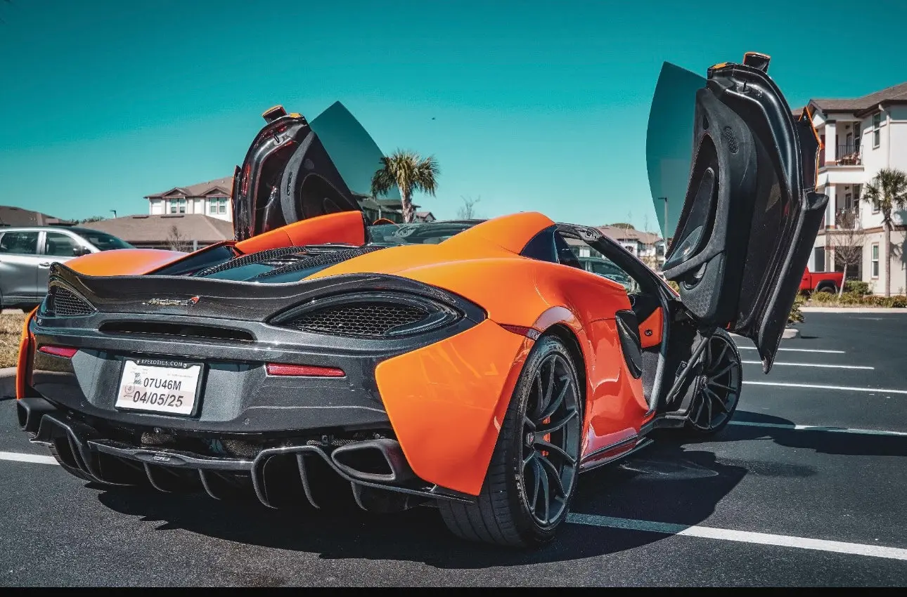 Orange McLaren sports car with butterfly doors open, parked in a sunny suburban lot, showcasing sleek aerodynamic design and black alloy wheels.