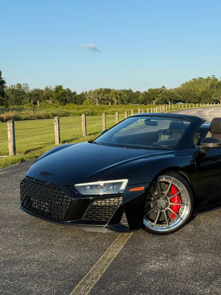 Sleek black Audi R8 convertible sports car with red brake calipers and alloy wheels parked on scenic road.