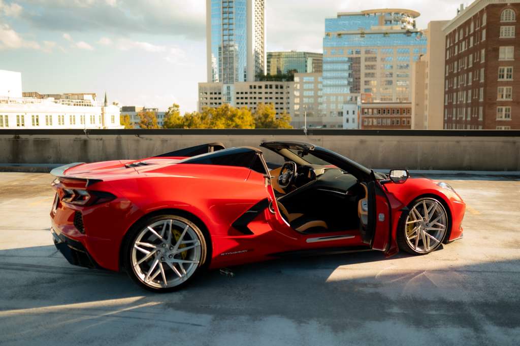 Red convertible sports car with open door and luxury interior, parked on rooftop with city skyline background, high-performance coupe vehicle for sale.