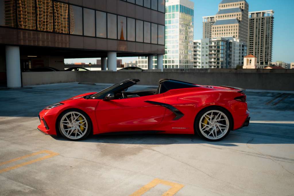 Red convertible sports car parked on rooftop with city skyline in background, luxury performance vehicle with sleek aerodynamic design.