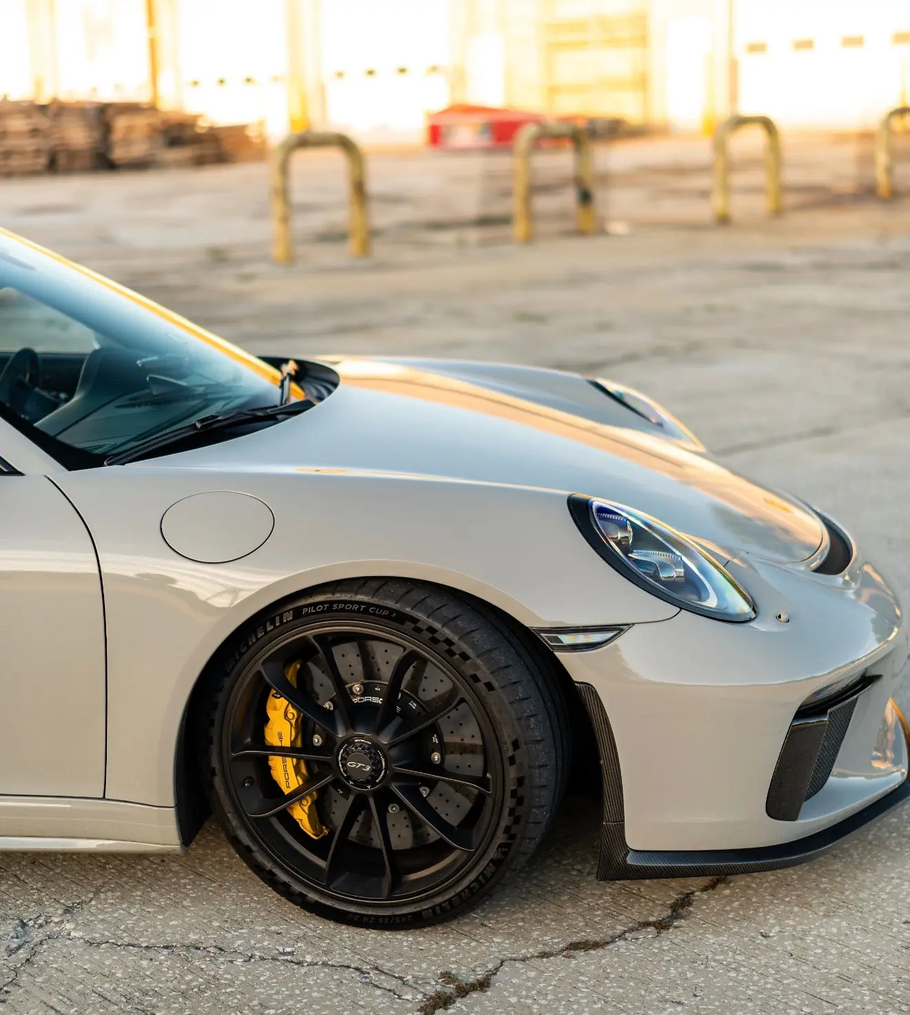 Front side view of a white Porsche 911 GT3 sports car featuring black alloy wheels, yellow brake calipers, and Michelin Pilot Sport Cup 2 tires on a textured concrete surface.