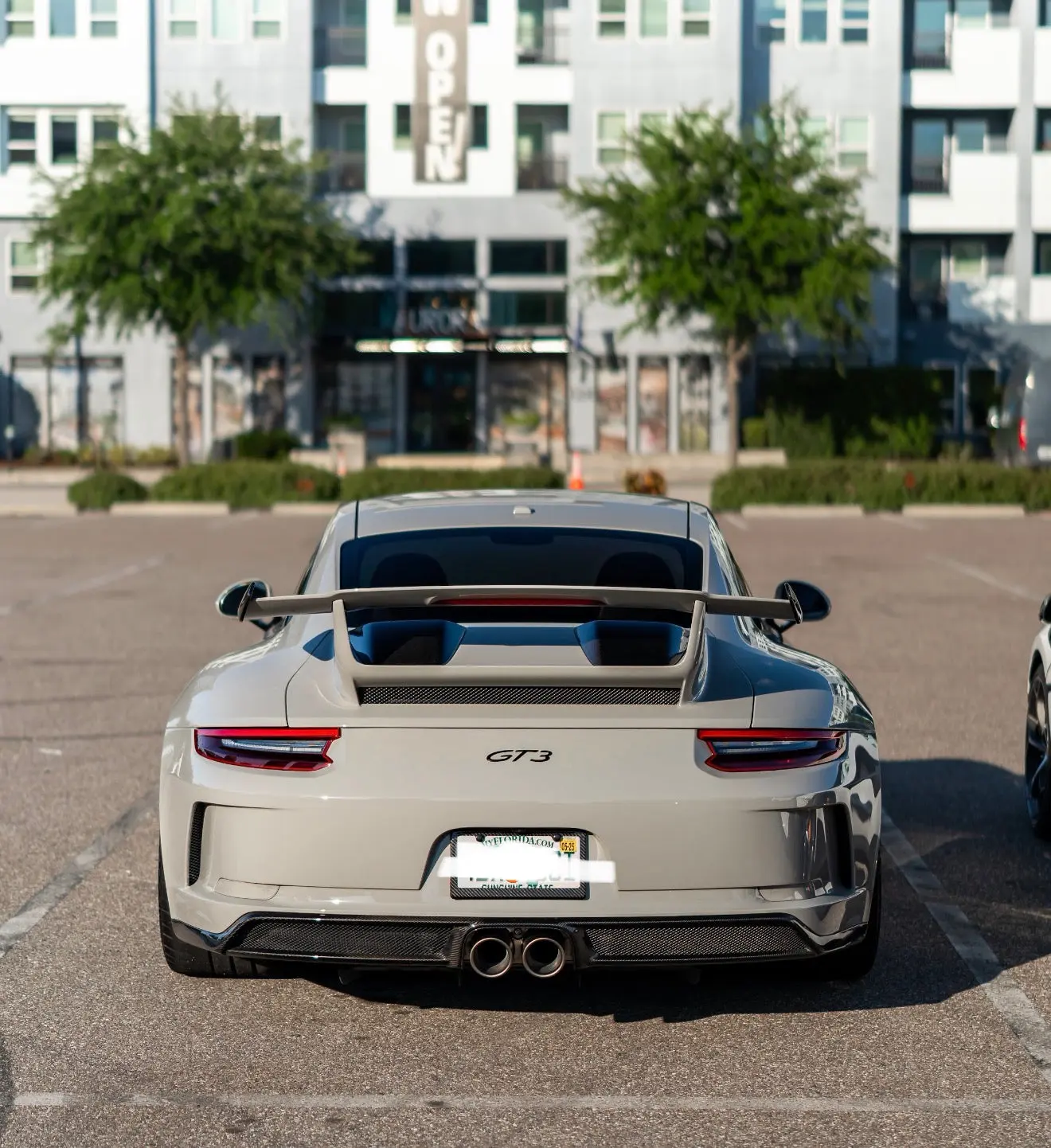 Rear view of white Porsche 911 GT3 sports car with carbon fiber rear diffuser and spoiler, parked in urban setting, high-performance luxury vehicle.