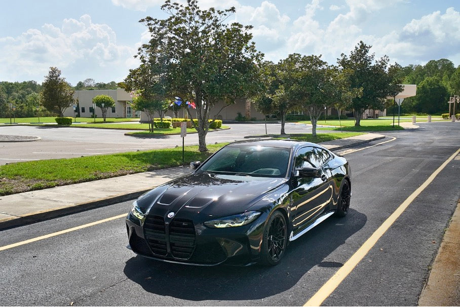 Sleek black BMW M4 sports car parked on a sunny suburban street, showcasing its aggressive front grille, aerodynamic design, and premium performance features.