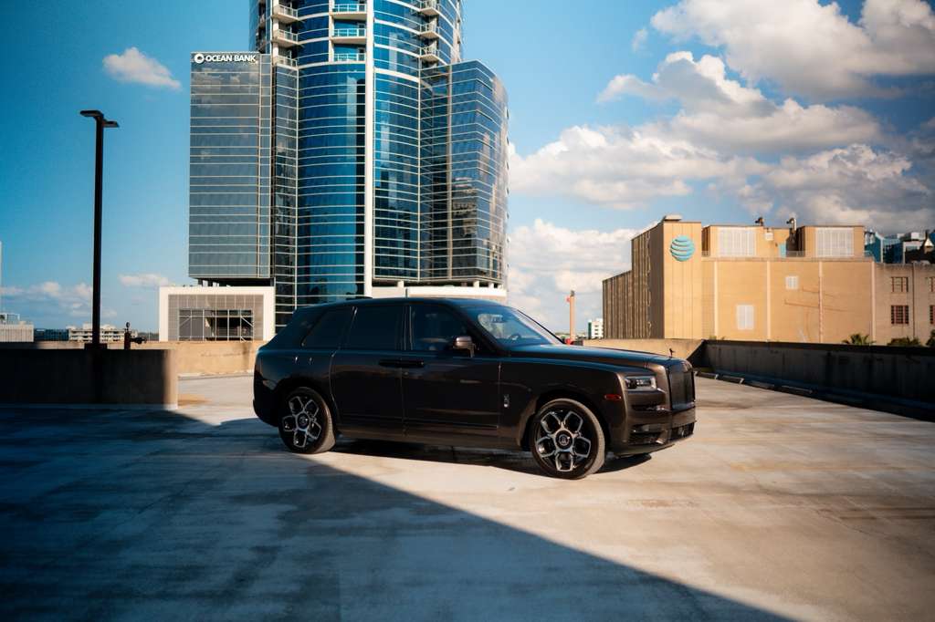 Luxury black Rolls-Royce SUV parked on urban rooftop with modern city skyline, premium executive car, high-end luxury vehicle for sale.