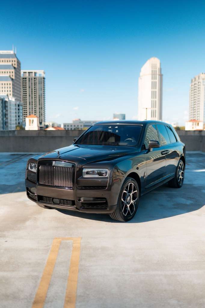 Black luxury Rolls-Royce Cullinan SUV parked on rooftop with city skyline, premium high-end luxury car, elegant exterior design.