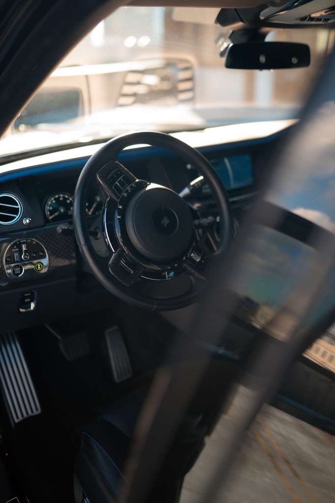 Interior view of a luxury Rolls-Royce car steering wheel and dashboard, featuring premium black leather, advanced digital instrument panel, and elegant design details for a high-end driving experience.