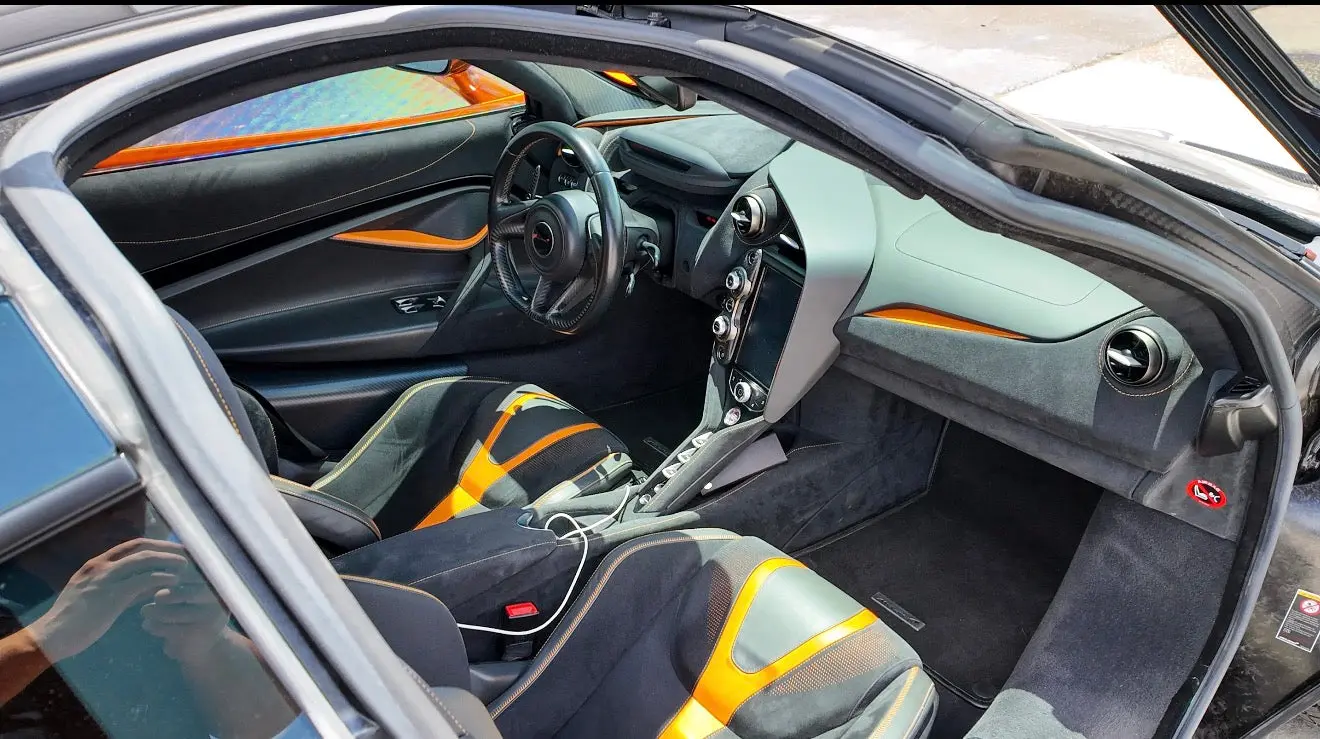 Luxury sports car interior featuring black and orange leather seats, modern dashboard with touchscreen display, and ergonomic steering wheel design.