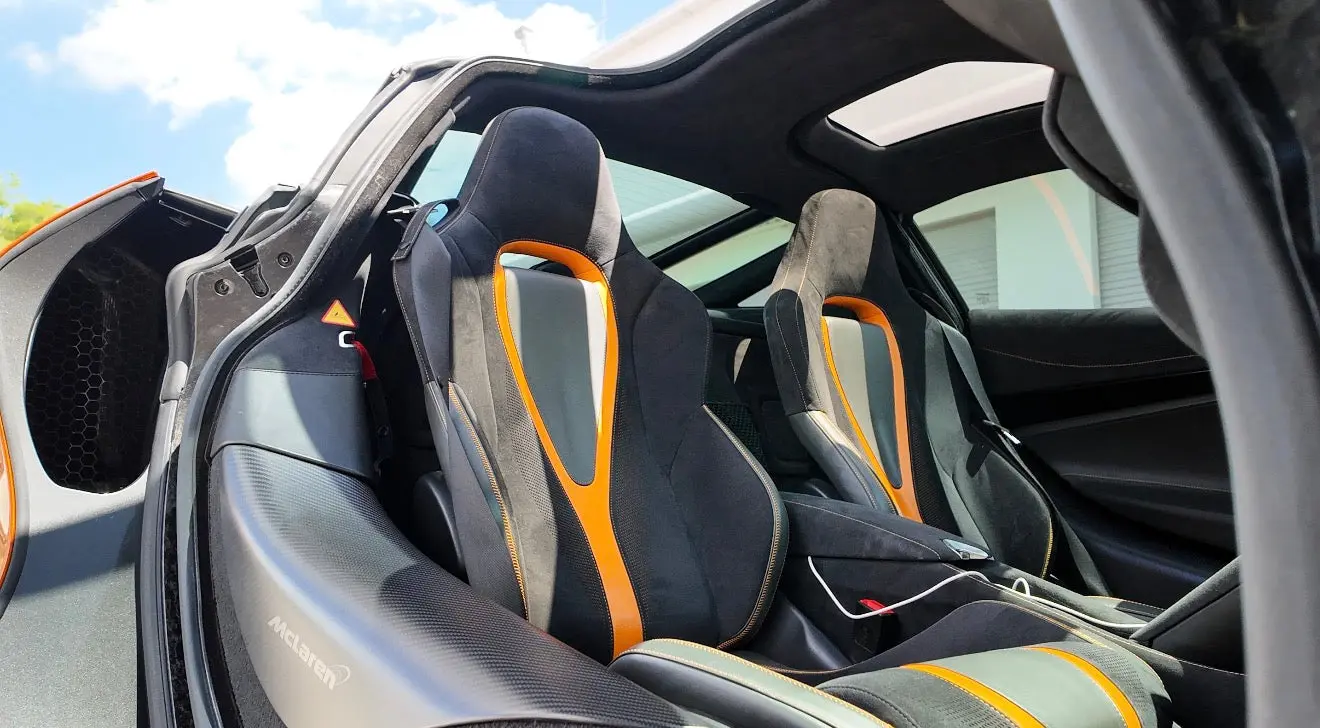 Interior view of McLaren sports car featuring black and orange leather racing seats with carbon fiber accents and panoramic sunroof.