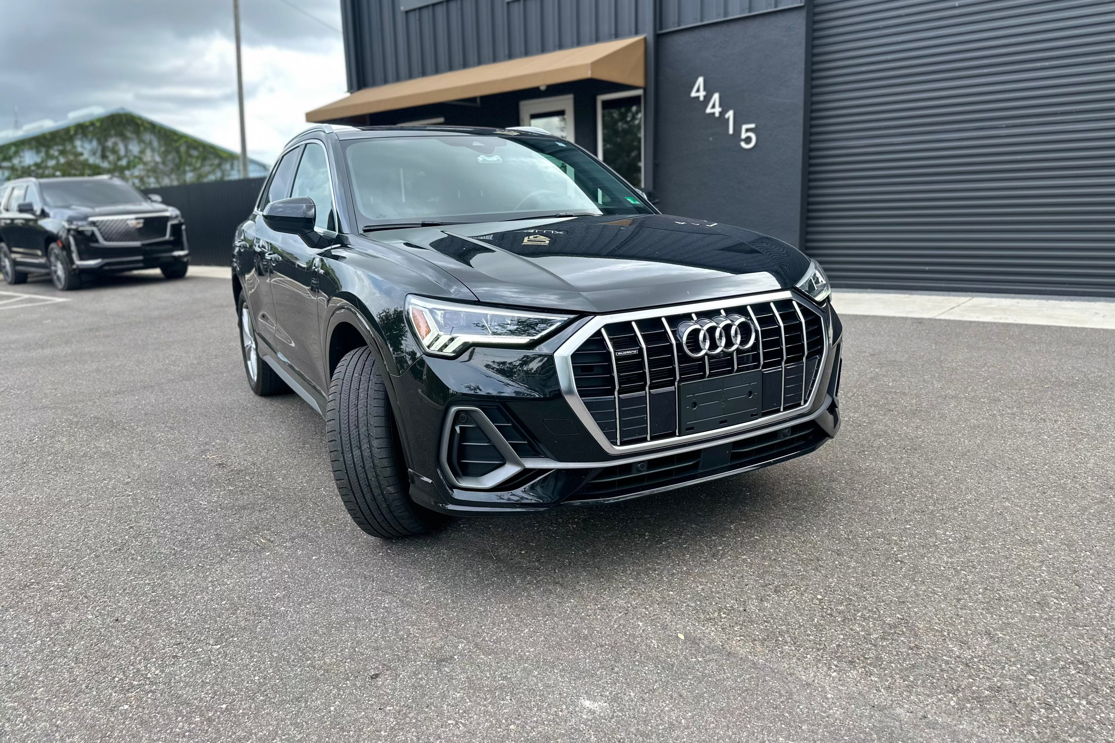Black Audi Q3 compact luxury SUV parked outside modern building, featuring bold front grille and LED headlights, ideal for premium crossover buyers.