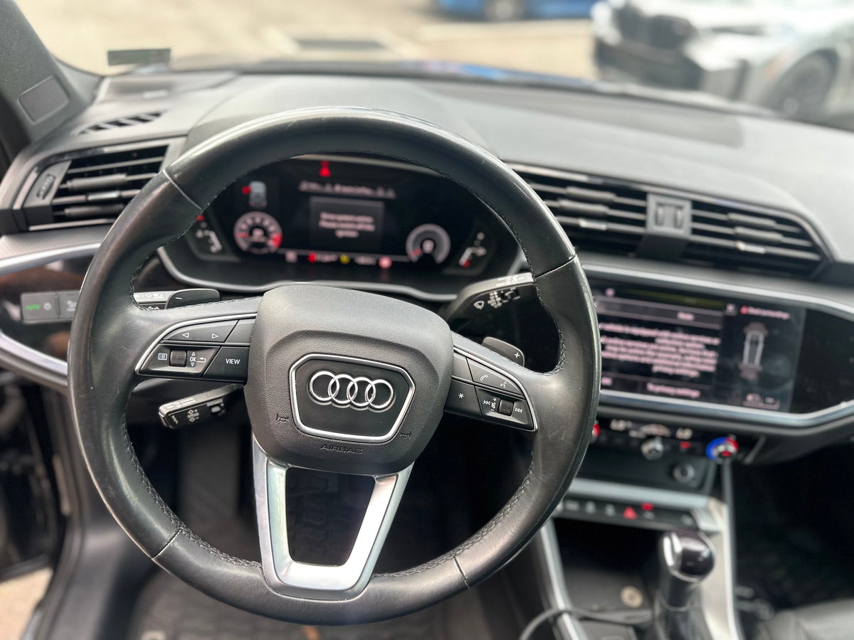 Close-up of black leather Audi steering wheel with multifunction buttons and digital dashboard display in luxury car interior