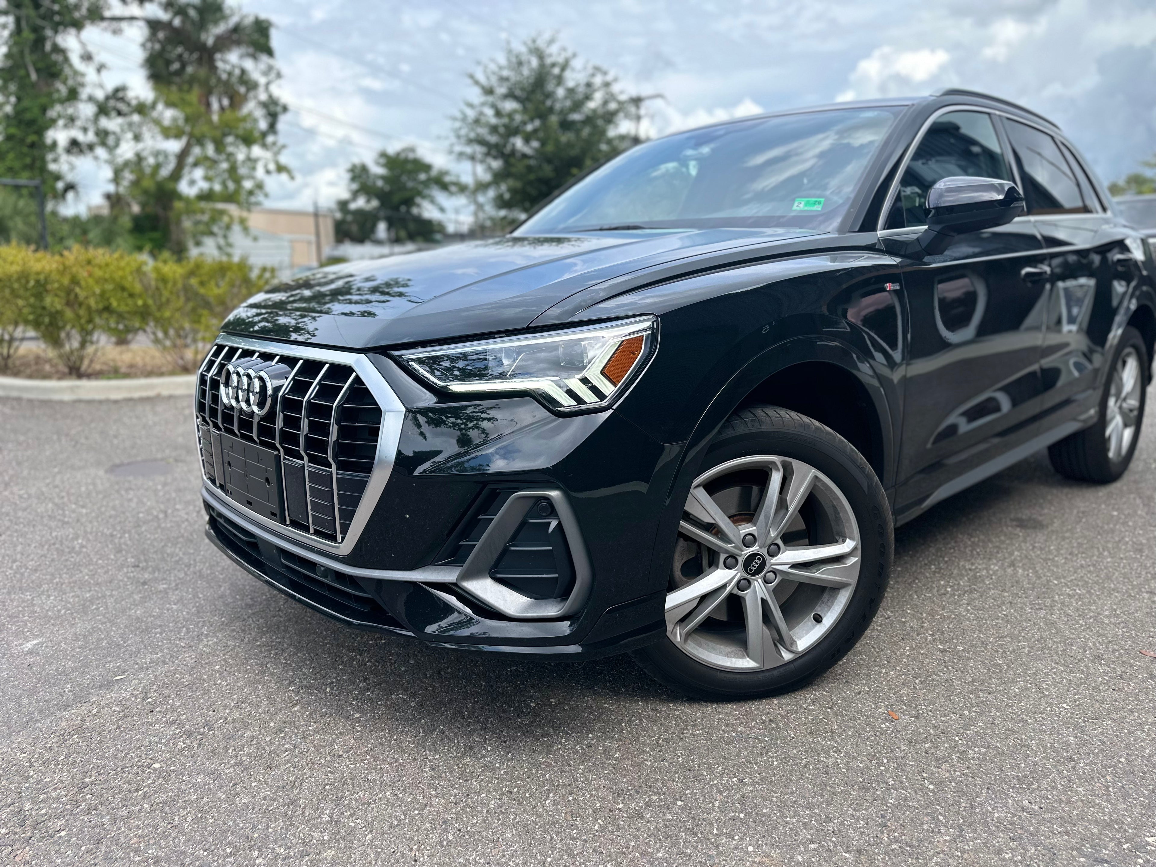 Black Audi Q3 luxury compact SUV with alloy wheels parked outdoors under cloudy sky, modern design crossover vehicle for sale.