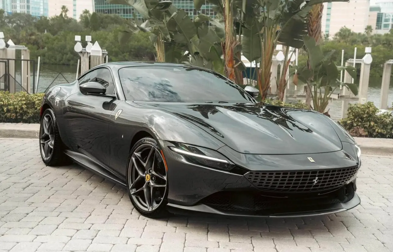Sleek black luxury Ferrari sports car with aerodynamic design and alloy wheels, parked on a stone driveway by waterfront, high-performance exotic vehicle.