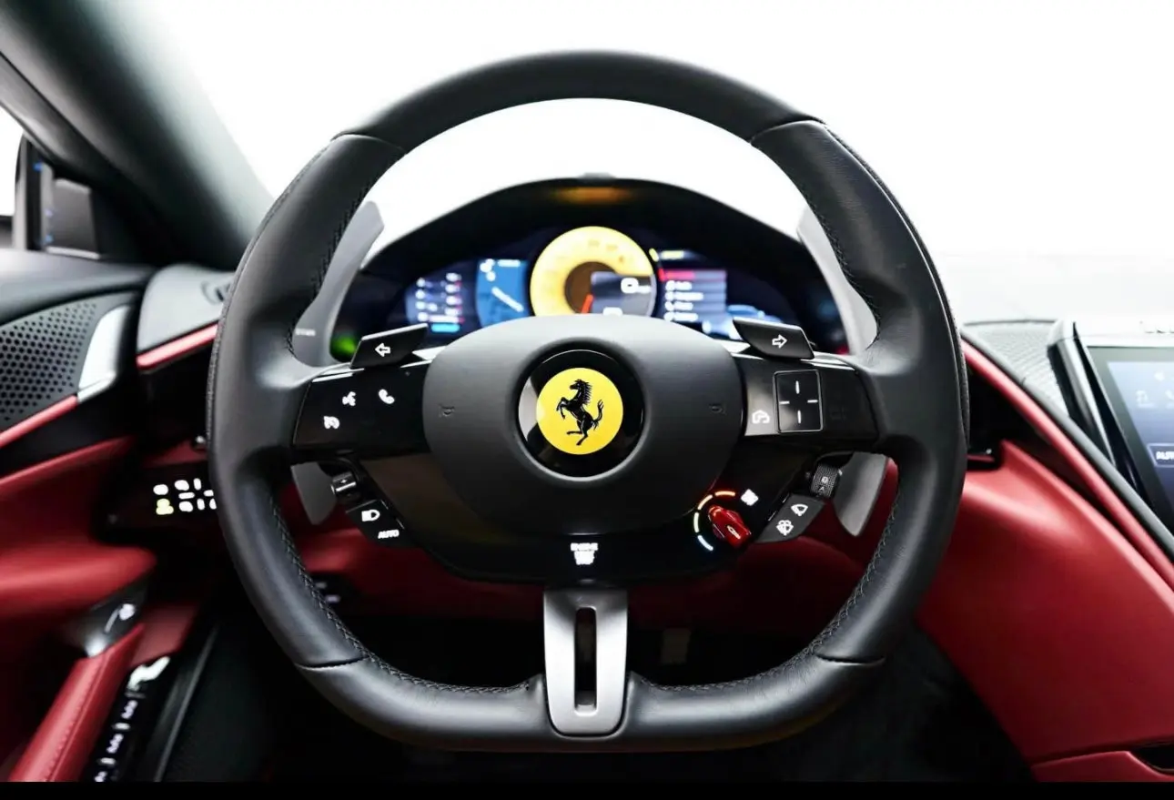 Black leather Ferrari steering wheel with multifunction controls and red interior dashboard, luxury sports car steering wheel close-up.