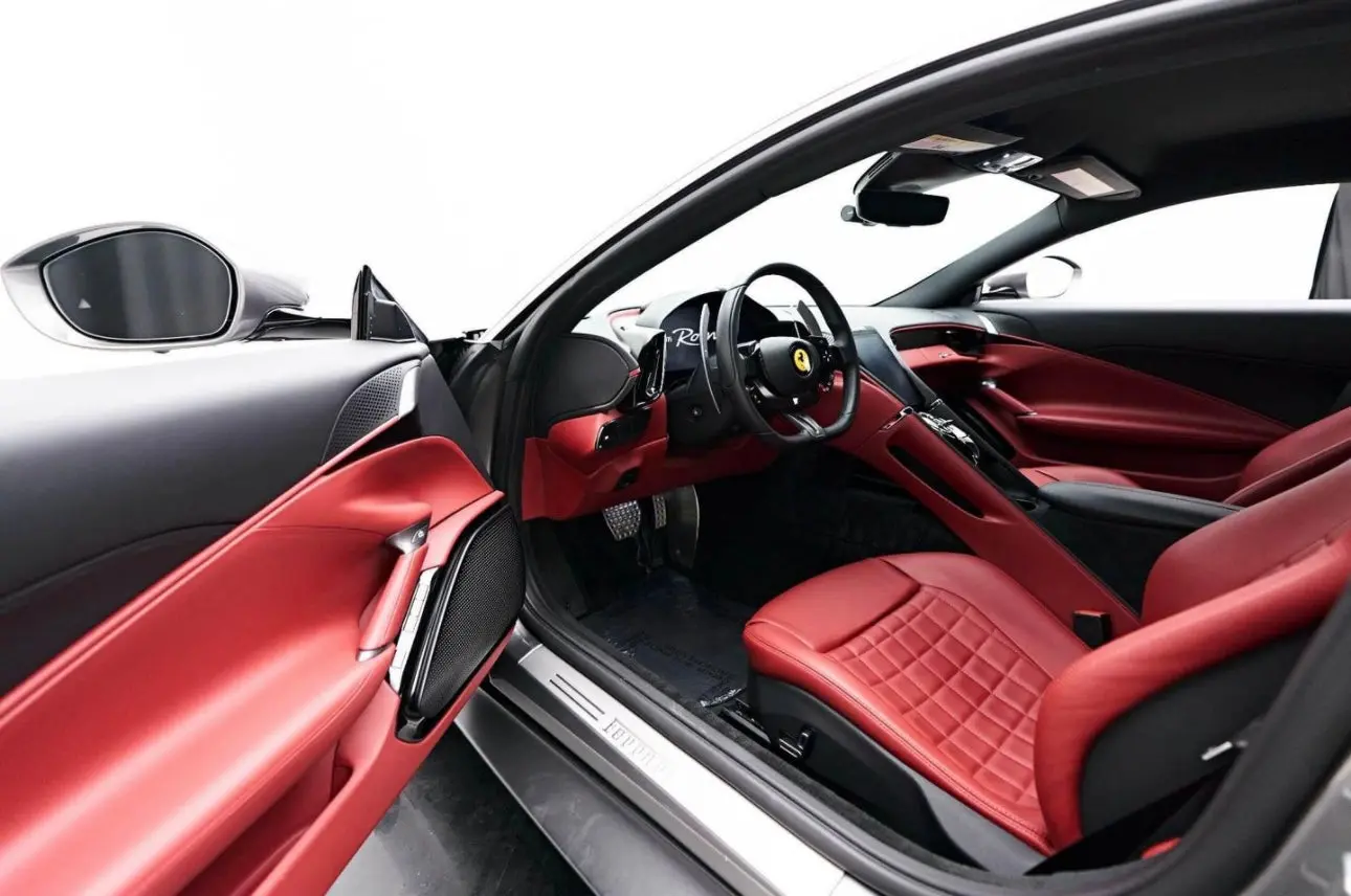 Luxury sports car interior featuring red leather seats and modern black dashboard with Ferrari logo steering wheel and advanced infotainment system.