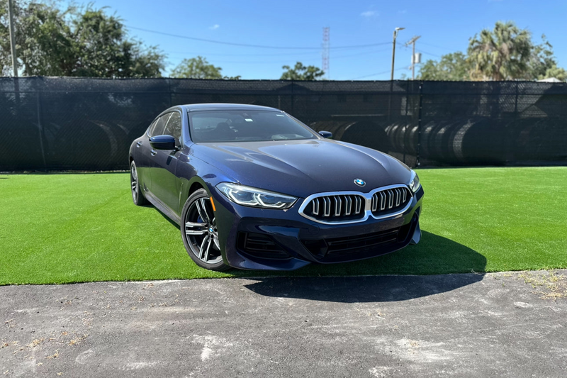 Blue BMW 8 Series luxury sports car parked on green grass with sleek aerodynamic design and LED headlights.