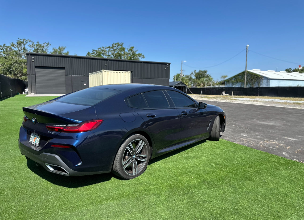 Dark blue BMW 8 Series Gran Coupe luxury sports sedan parked on green grass with sleek alloy wheels and tinted windows under clear blue sky.