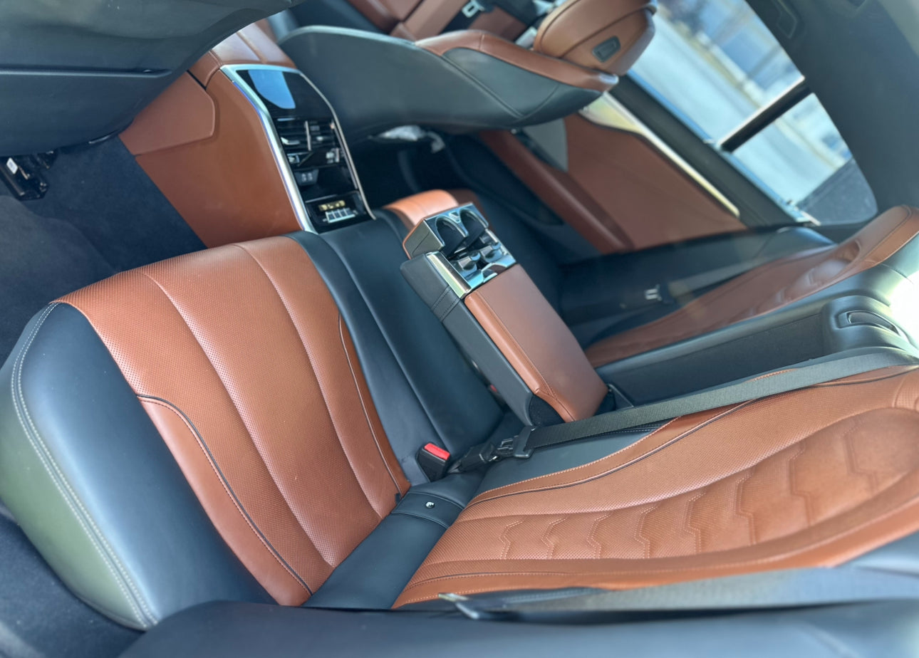 Luxury car rear seats with brown and black leather upholstery, featuring center armrest and cup holders, premium automotive interior design.