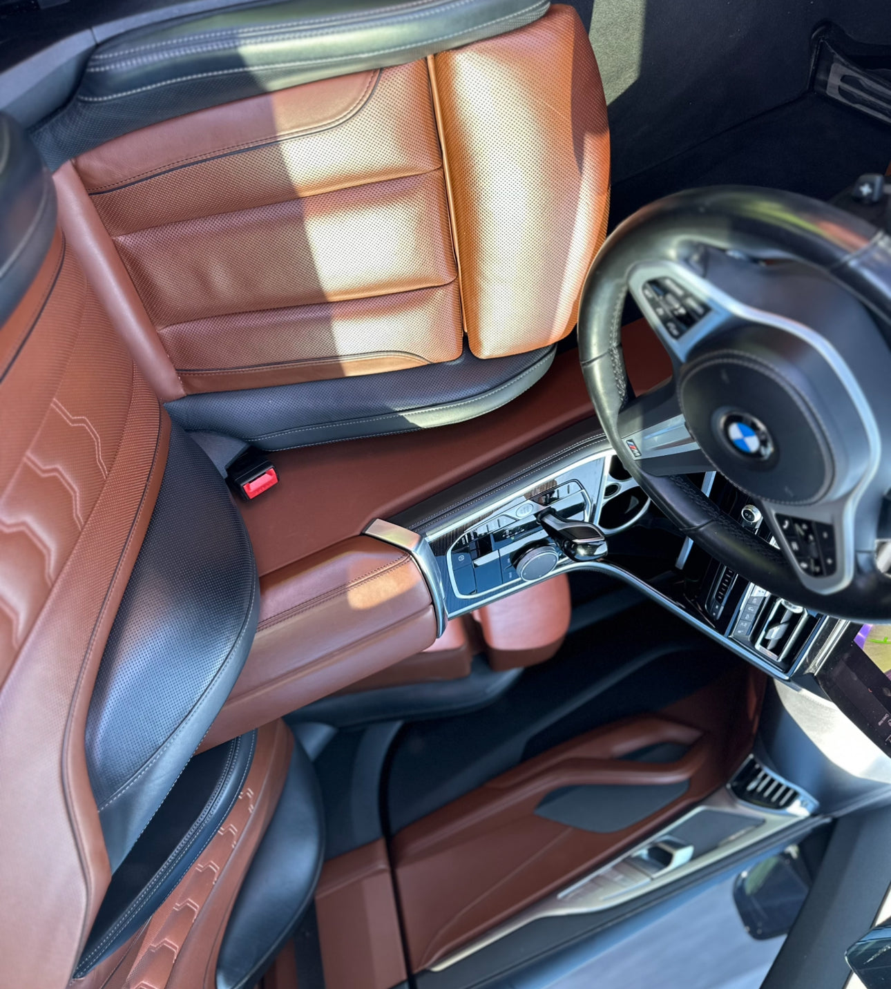 Close-up of luxury BMW car interior featuring brown and black leather seats, modern center console with gear shift, and multifunction steering wheel, showcasing premium automotive design.
