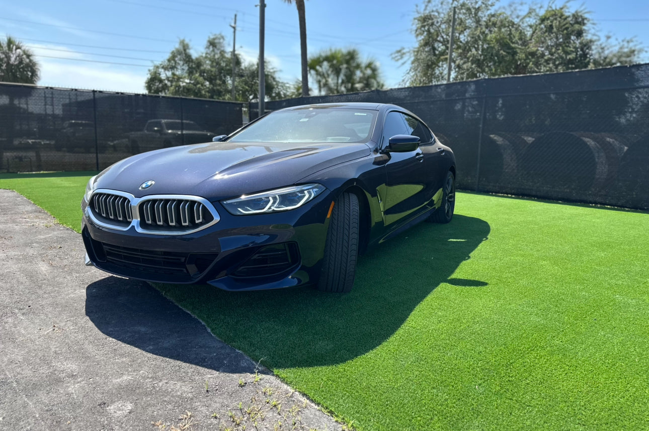 Sleek black BMW 8 Series luxury coupe parked on green grass with modern LED headlights and signature kidney grille, showcasing sporty design and premium performance.