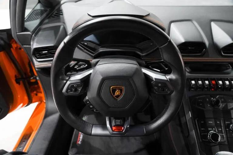 Black leather Lamborghini steering wheel with orange stitching, featuring sport car controls and luxury interior dashboard details.