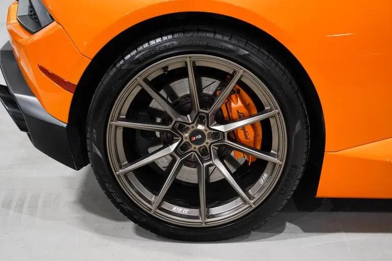 Close-up of a high-performance alloy wheel with multi-spoke design and orange Brembo brake caliper on a bright orange sports car tire.