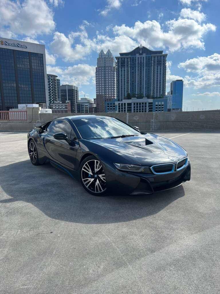 BMW i8 parked in downtown Orlando with skyscrapers in the background against a bright blue sky.