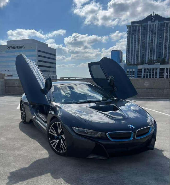 BMW i8 with futuristic scissor doors open against a city skyline, showcasing luxury and style.