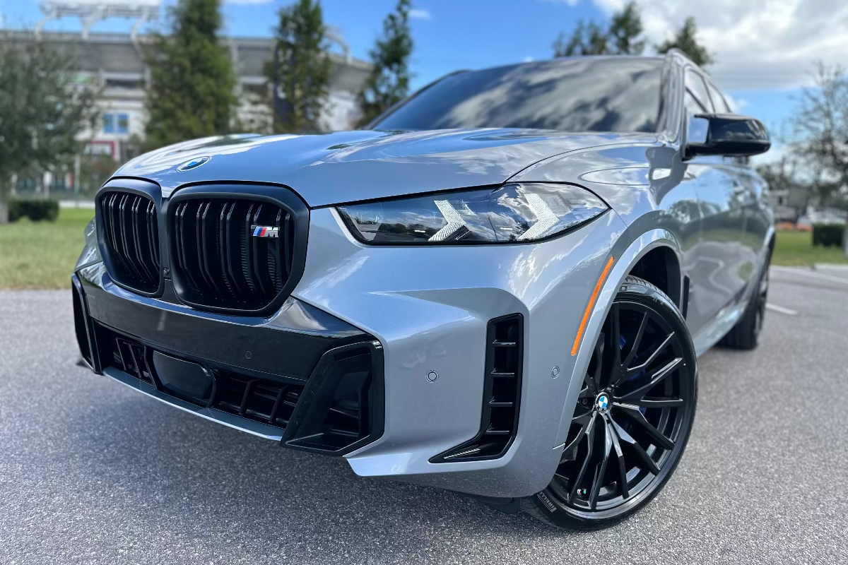 Front view of a sleek gray BMW X6 M SUV with black kidney grille, LED headlights, and black alloy wheels parked outdoors on pavement.