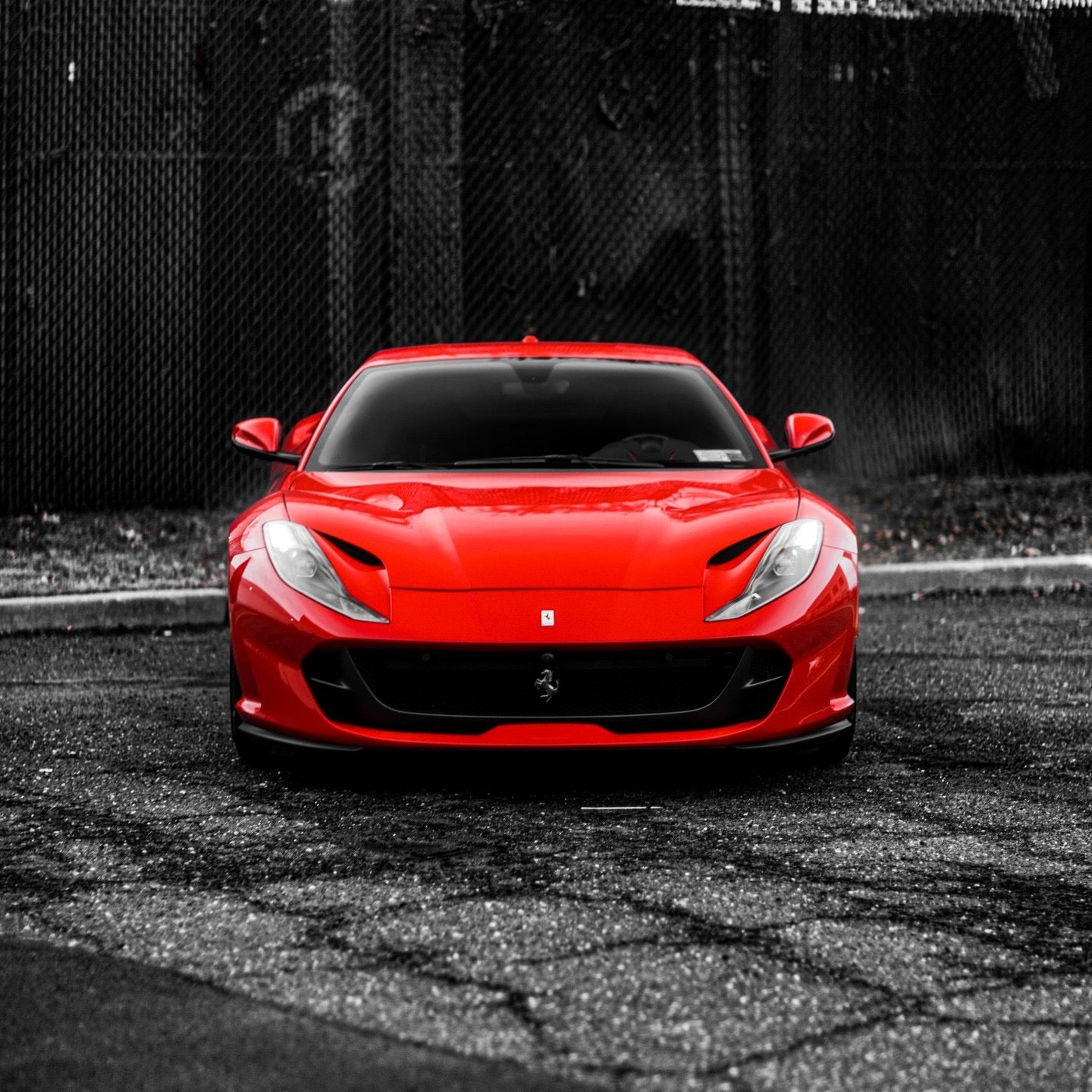 Front view of a red Ferrari sports car parked on asphalt, showcasing sleek aerodynamic design and high-performance luxury vehicle features.