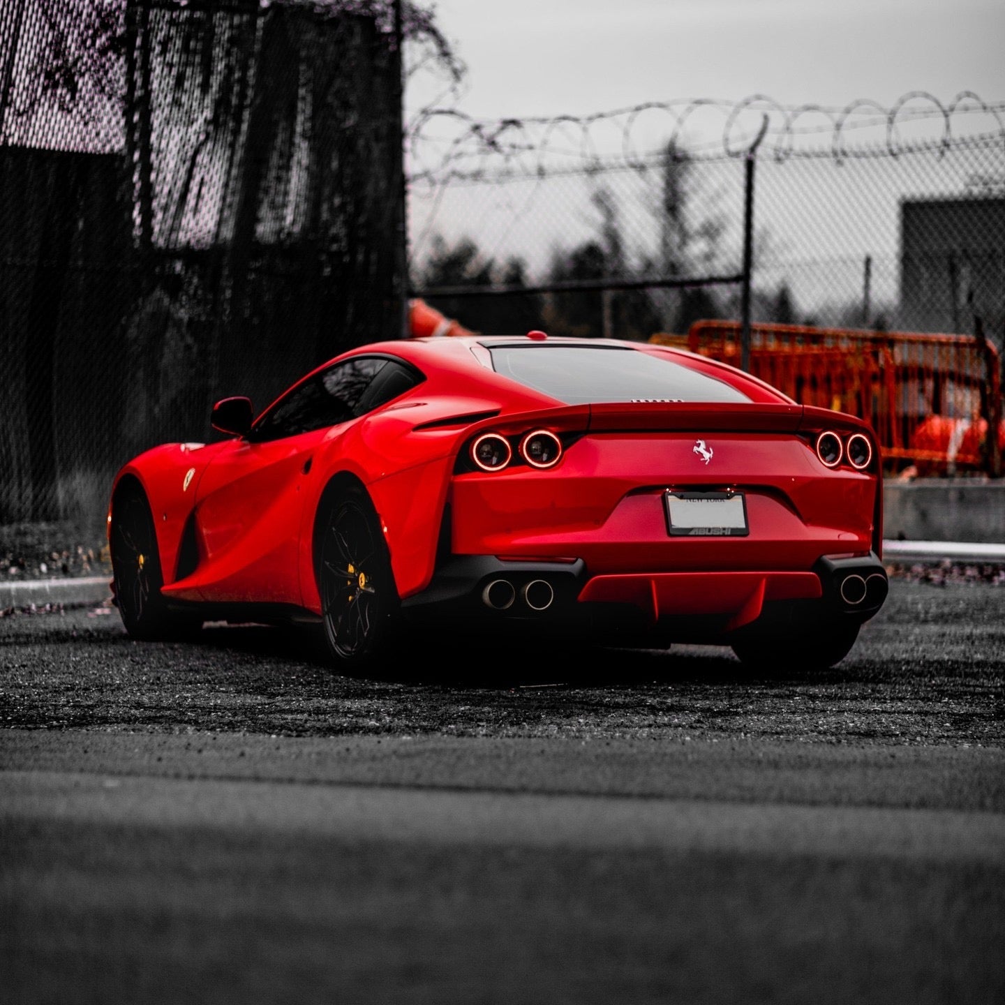 Red Ferrari sports car with sleek aerodynamic design and quad exhaust pipes, parked on urban asphalt road.