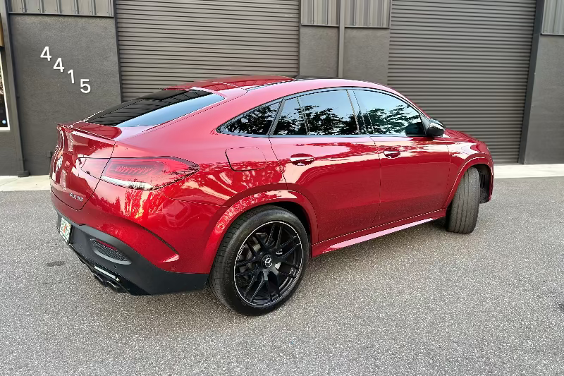 Red Mercedes-Benz GLE 53 AMG Coupe with black alloy wheels, sporty design, and tinted windows parked on asphalt.