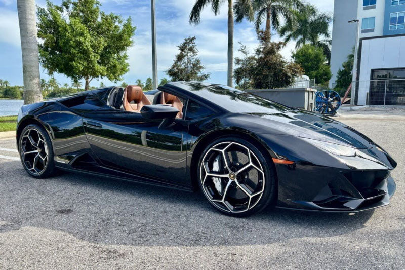 Black sports car on a street with palm trees and buildings in the background