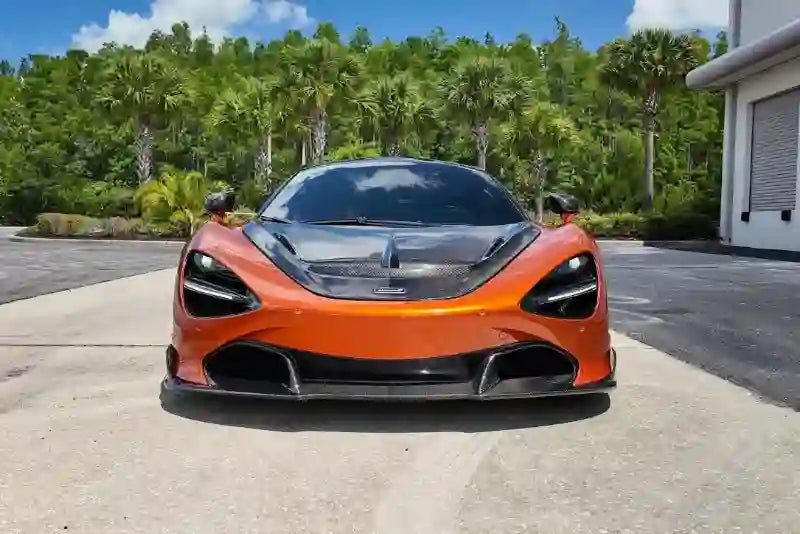 Orange sports car parked on a driveway with trees and a building in the background
