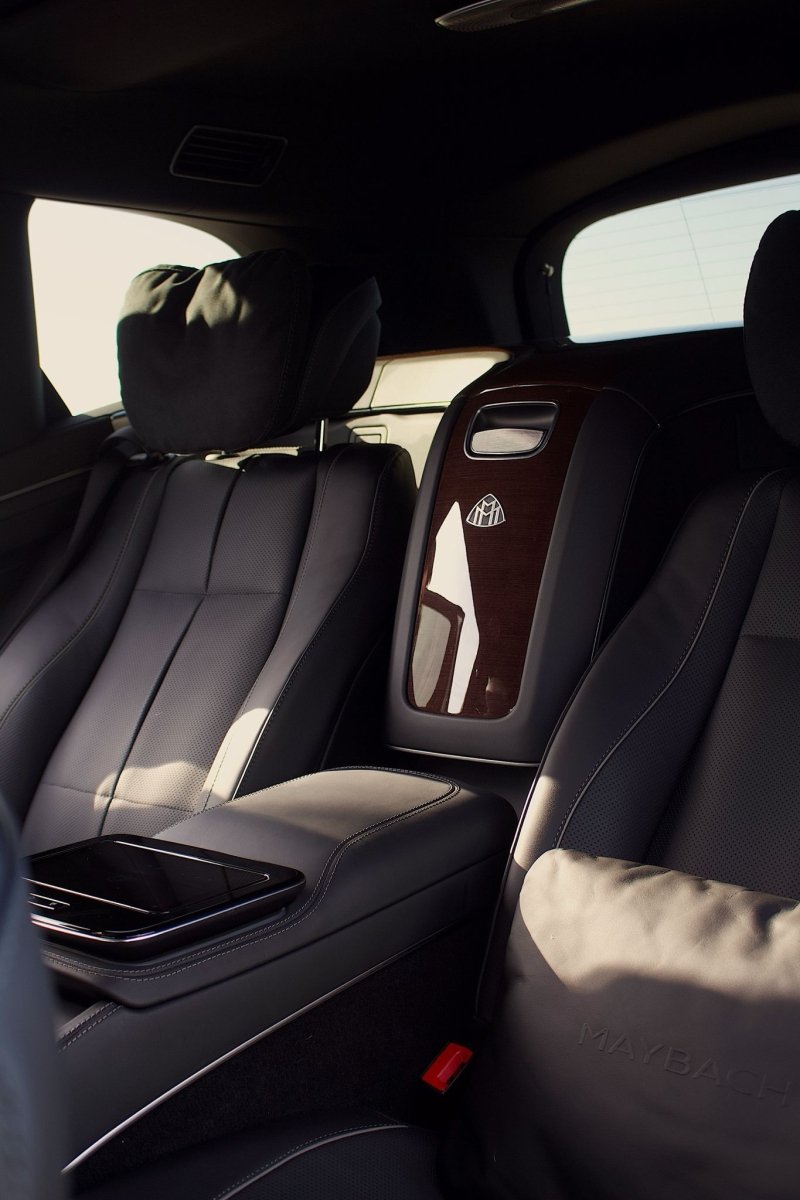 Luxury Maybach car interior with black leather seats, wood trim accents, and plush headrest pillow.