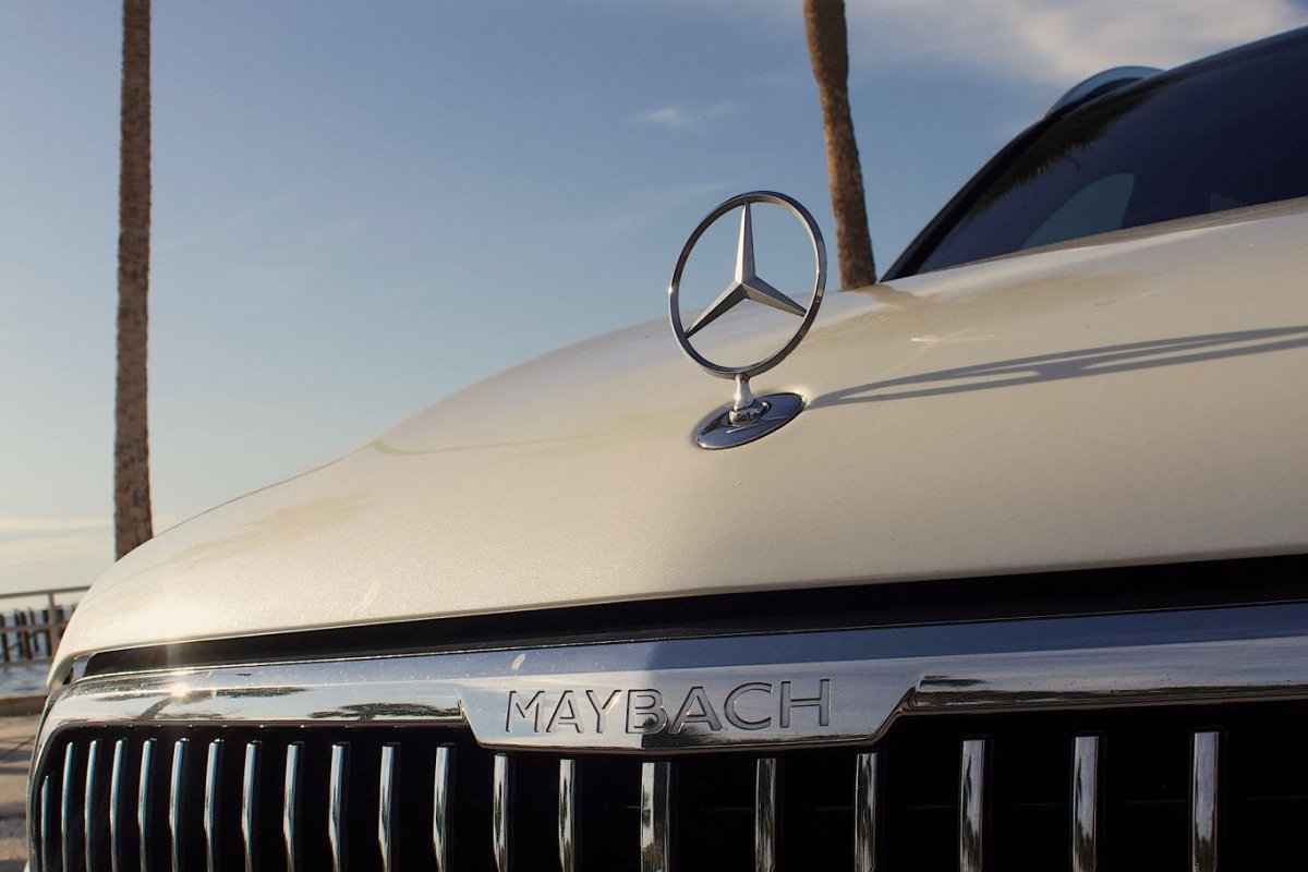 Close-up of luxury Mercedes Maybach front grille and iconic star hood ornament on white premium vehicle under clear sky, high-end luxury car detail.