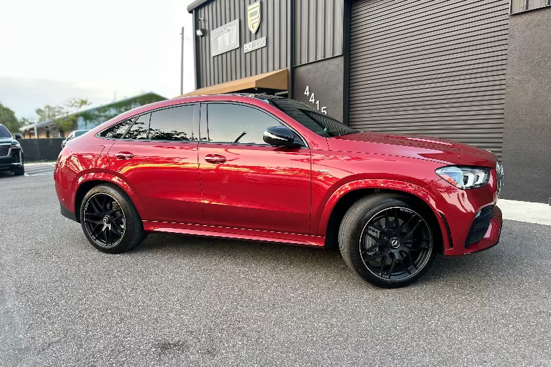 Red luxury Mercedes-Benz GLE Coupe with black alloy wheels and tinted windows parked outside modern industrial building.